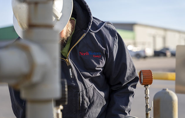 A natural gas worker inspects a pipe. The NorthWestern Energy logo can be seen on his shirt.